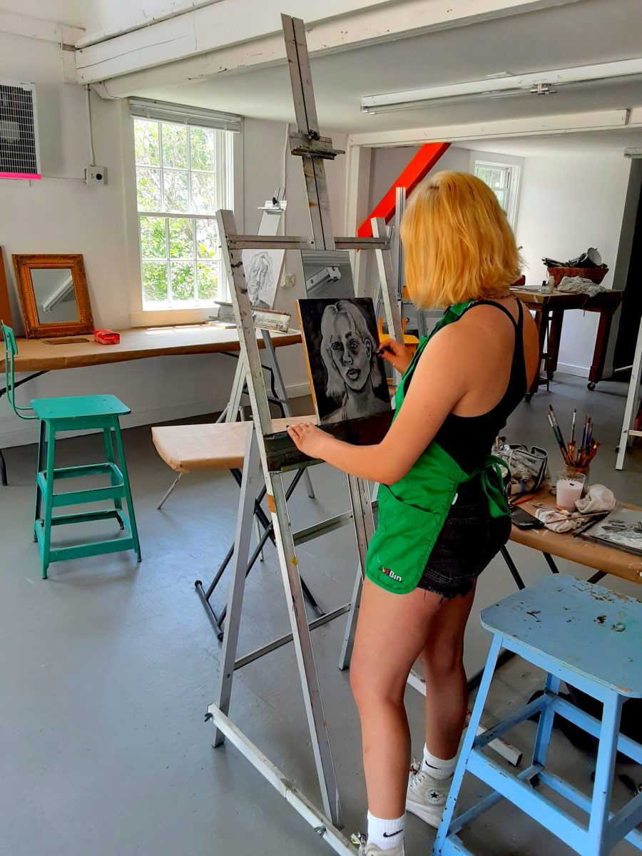 A girl is sketching a self portrait at an easel