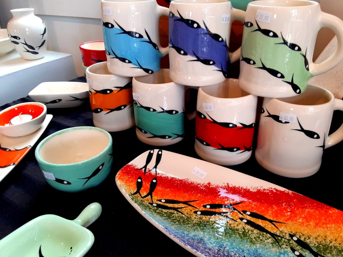Ceramic cups and plates are shown with colorful fish painted on them.