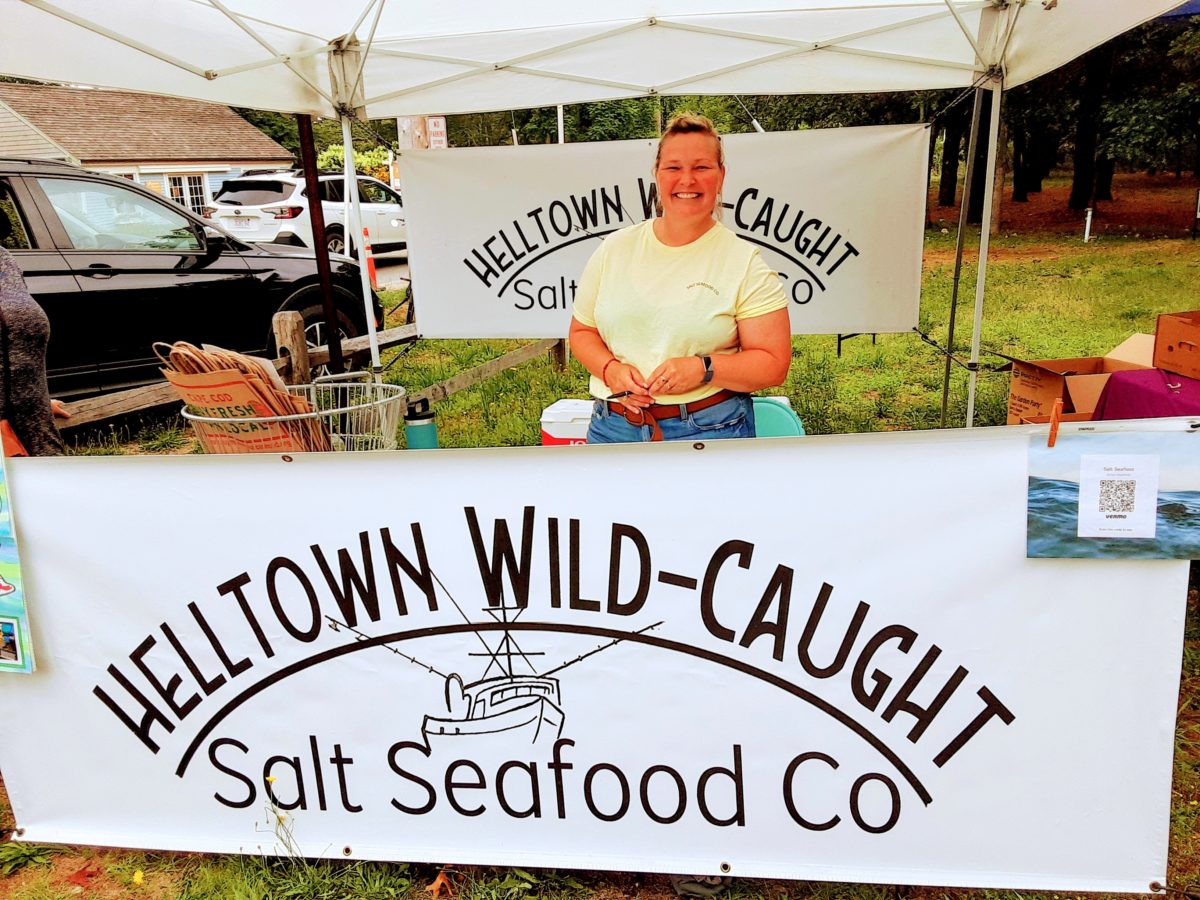 A woman stands behind a large banner selling fish