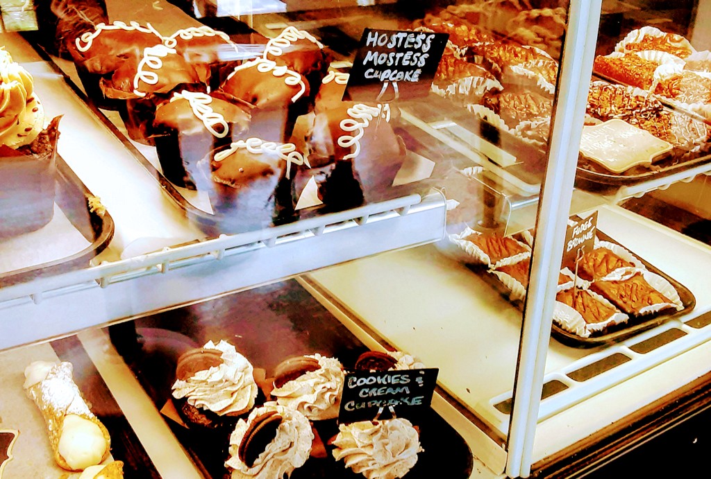 Cupcakes and pastries are displayed in a glass case.