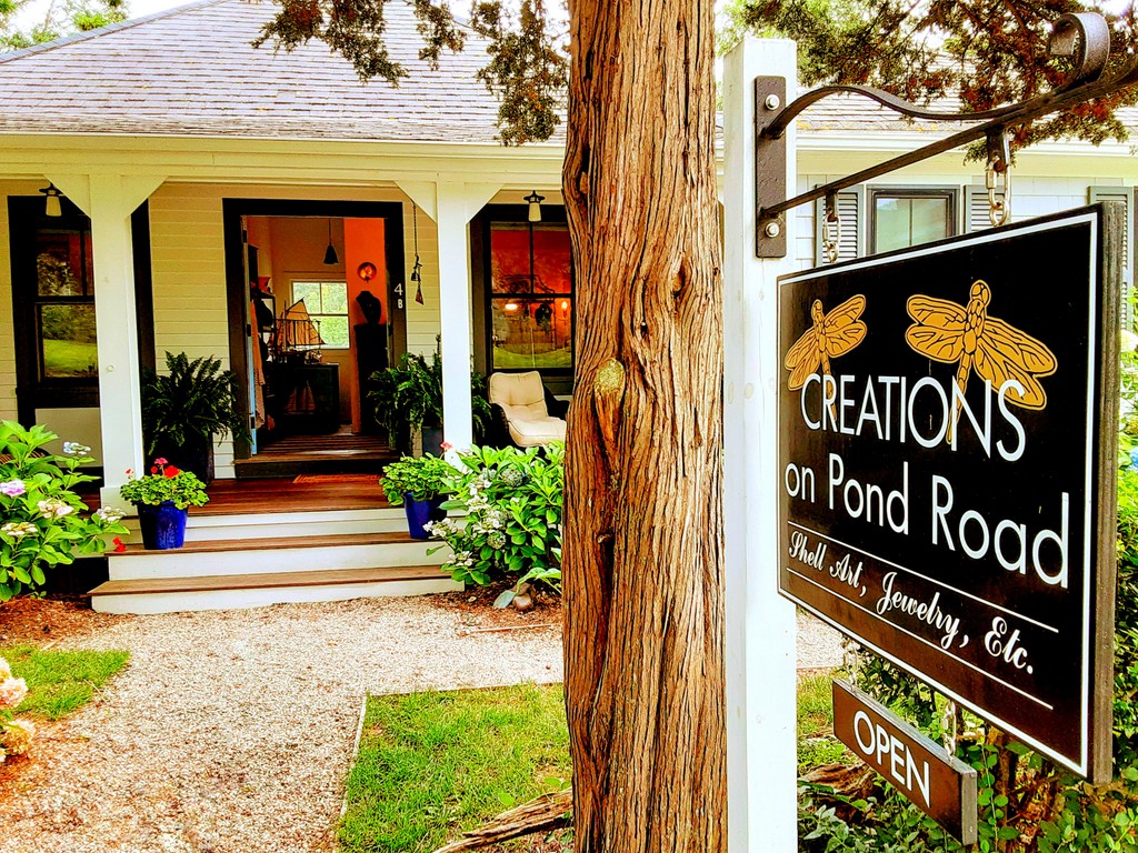 A sign in front of a house reads Creations on Pond Road